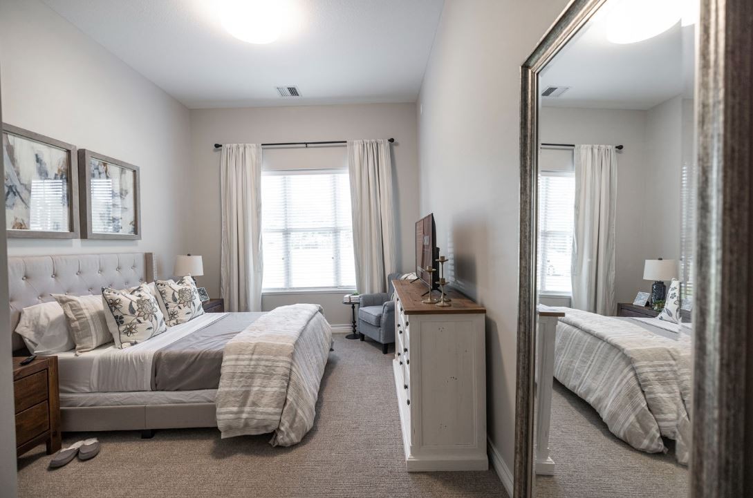 A modern bedroom with a large mirror, neatly arranged furniture, and neutral decor.