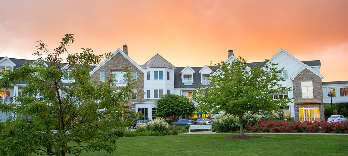 A charming residential building set against a vibrant sunset, surrounded by lush greenery and well-maintained lawns.