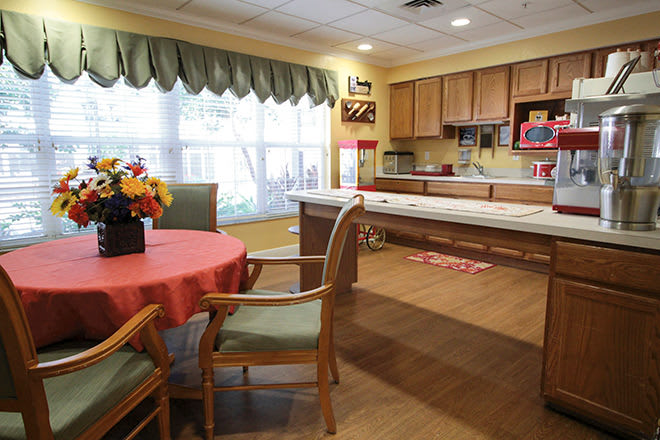 A cozy kitchen and dining area featuring a round table with chairs, cabinetry, and large windows with curtains.