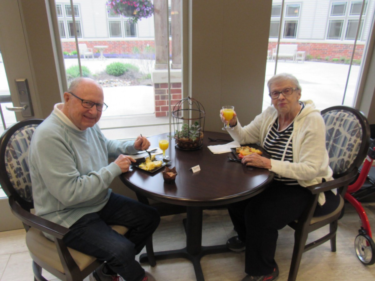 A senior couple enjoys a meal together at a small table by the window.