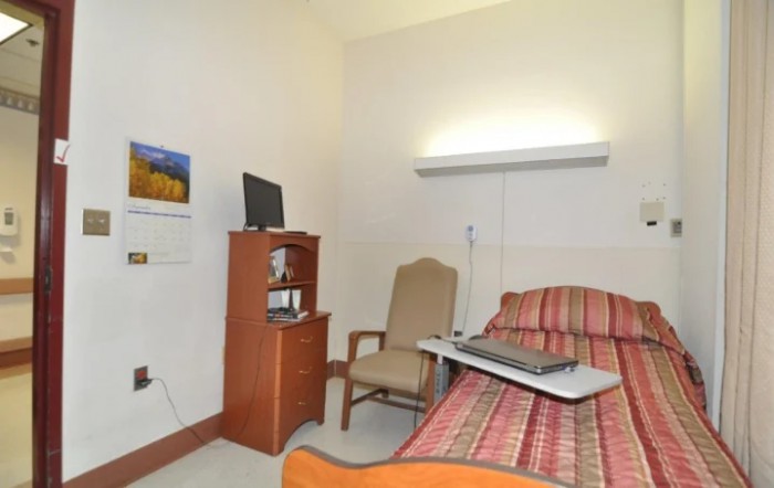 A small hospital room with a bed, chair, and television.
