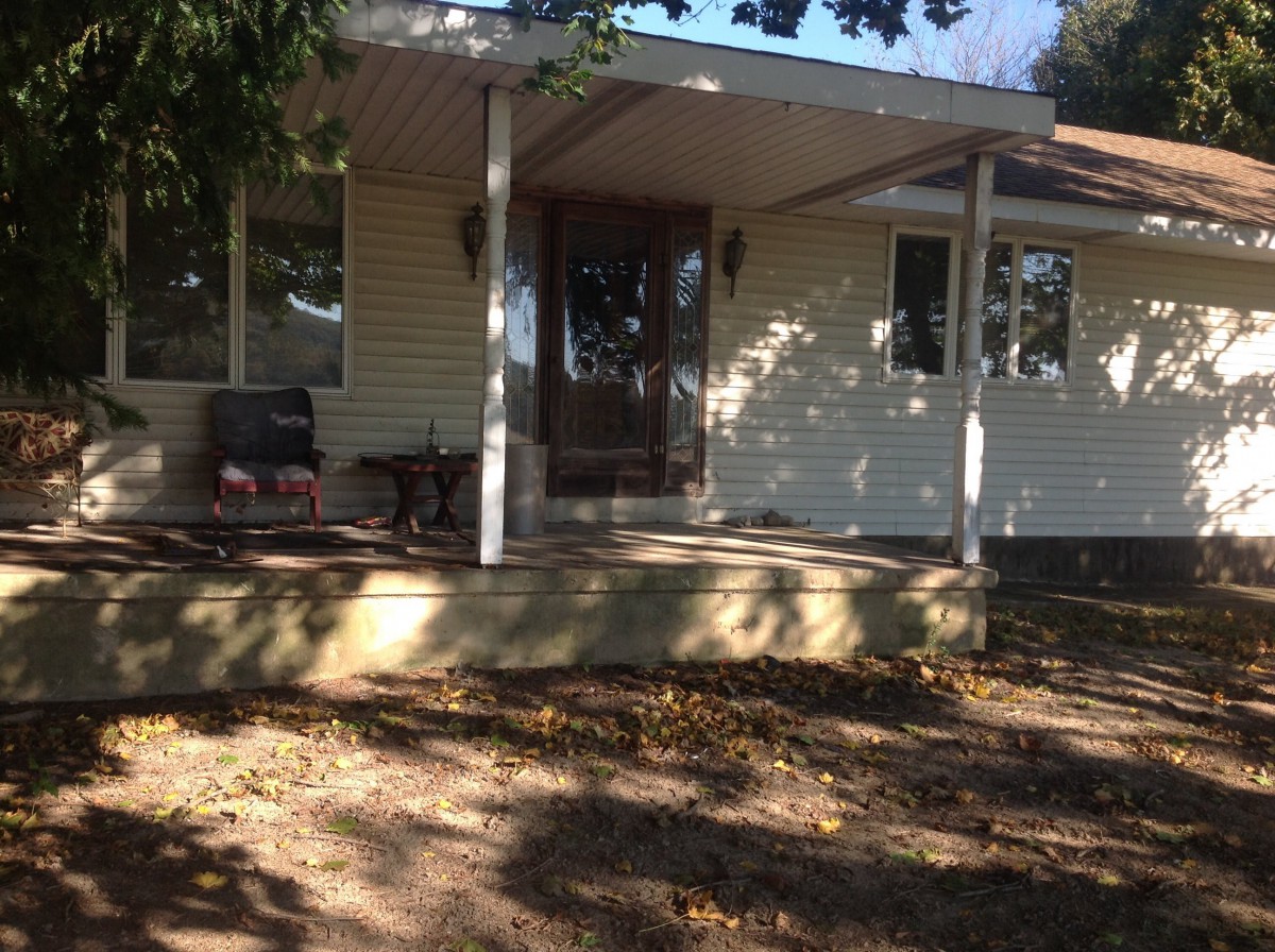 A sunny view of a house with a porch and steps, surrounded by trees.