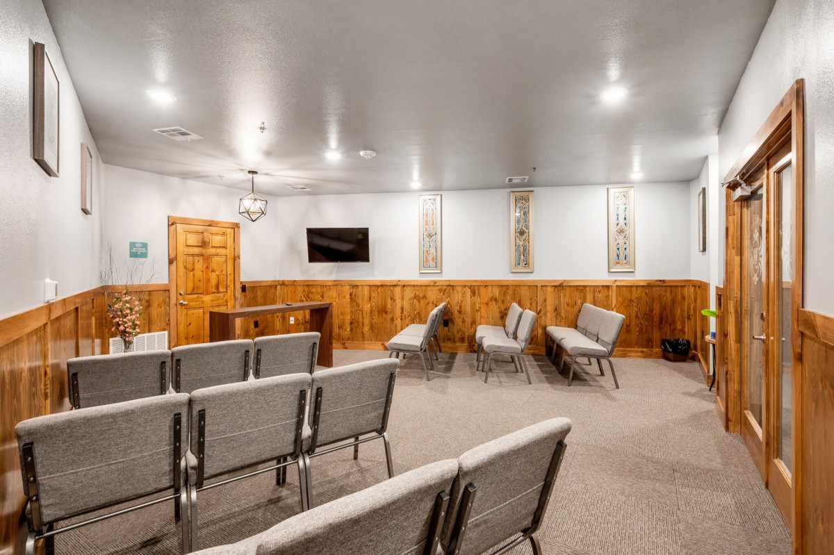 An empty meeting room with rows of chairs facing a television on the wall, featuring wood paneling and warm lighting.