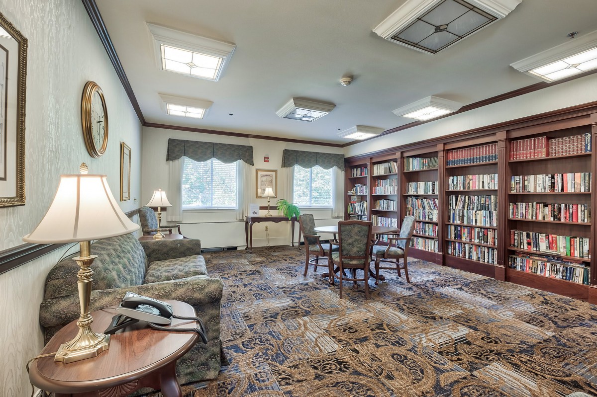 A cozy library room with bookshelves, a seating area, and natural light coming through the windows.
