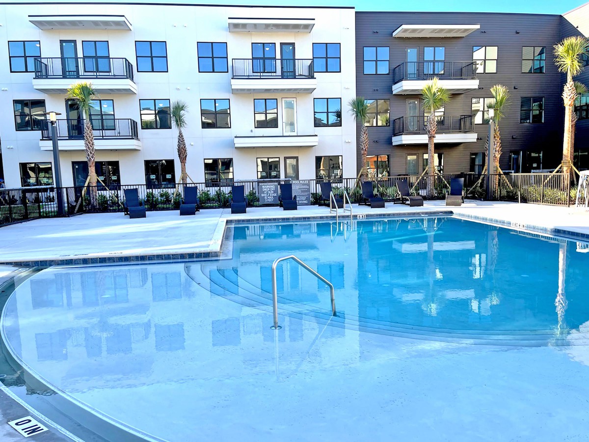 A modern apartment building overlooks a pristine outdoor swimming pool, surrounded by palm trees.