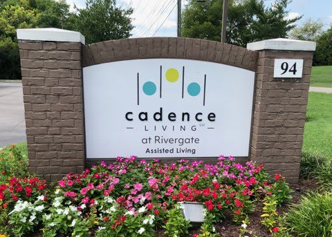 Sign for Cadence Living at Rivergate Assisted Living surrounded by colorful flowers.