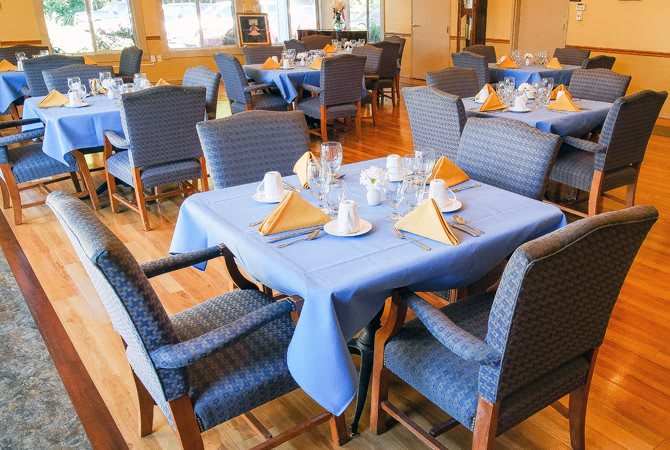 A restaurant dining area with tables set for guests, featuring blue tablecloths and neatly arranged napkins and glasses.