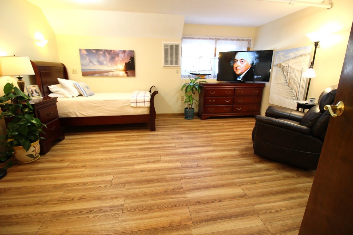 A cozy bedroom with wooden flooring, featuring a bed, dresser, television, and seating area.