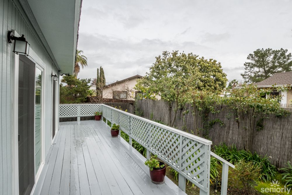 A spacious outdoor deck with potted plants overlooks a fenced suburban garden under an overcast sky.