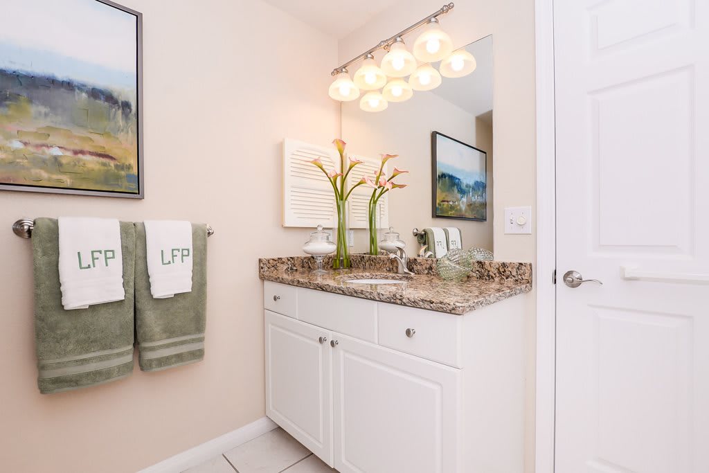 A modern bathroom with a granite countertop, neatly arranged towels, and decorative plants.