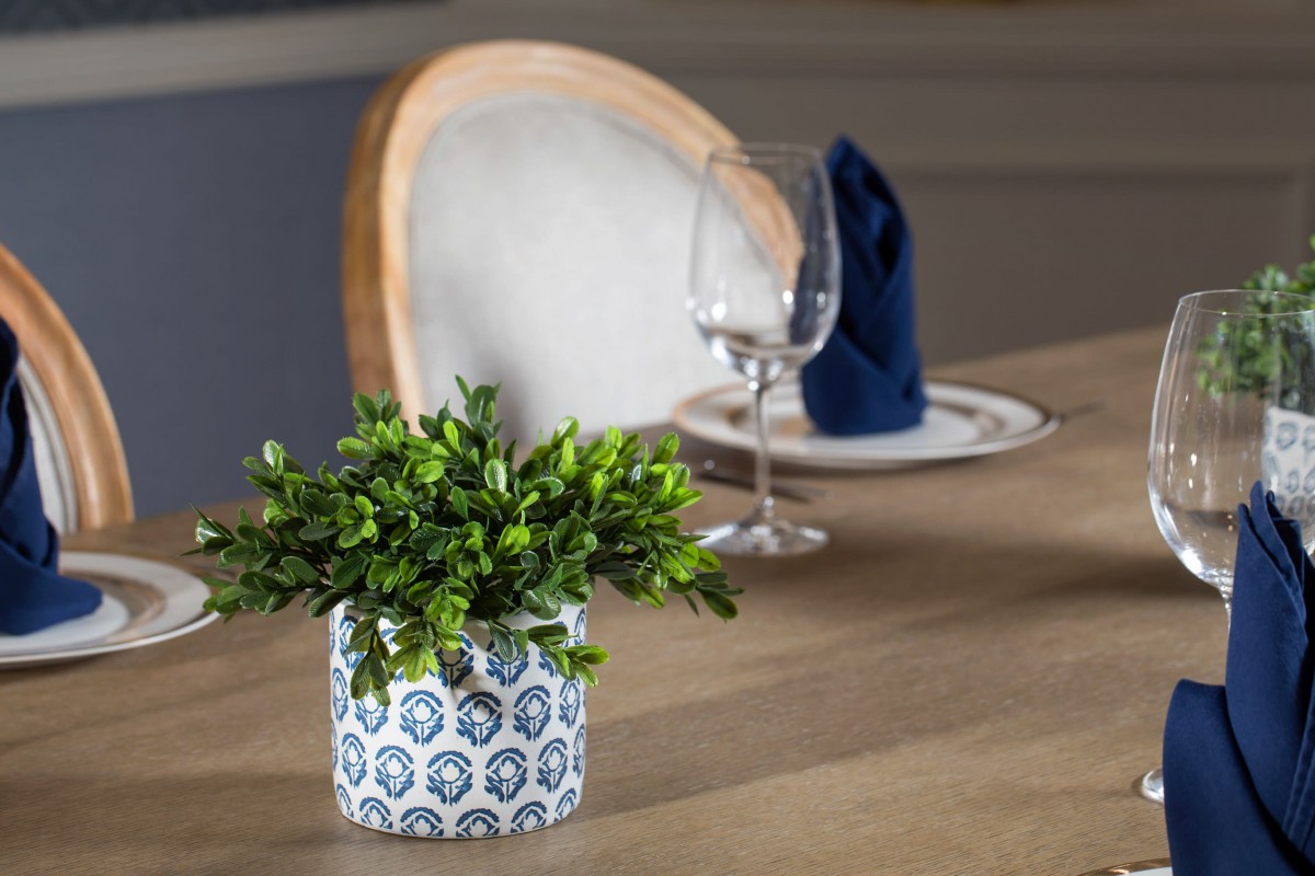 A dining table set with a decorative potted plant, wine glass, and folded napkin.