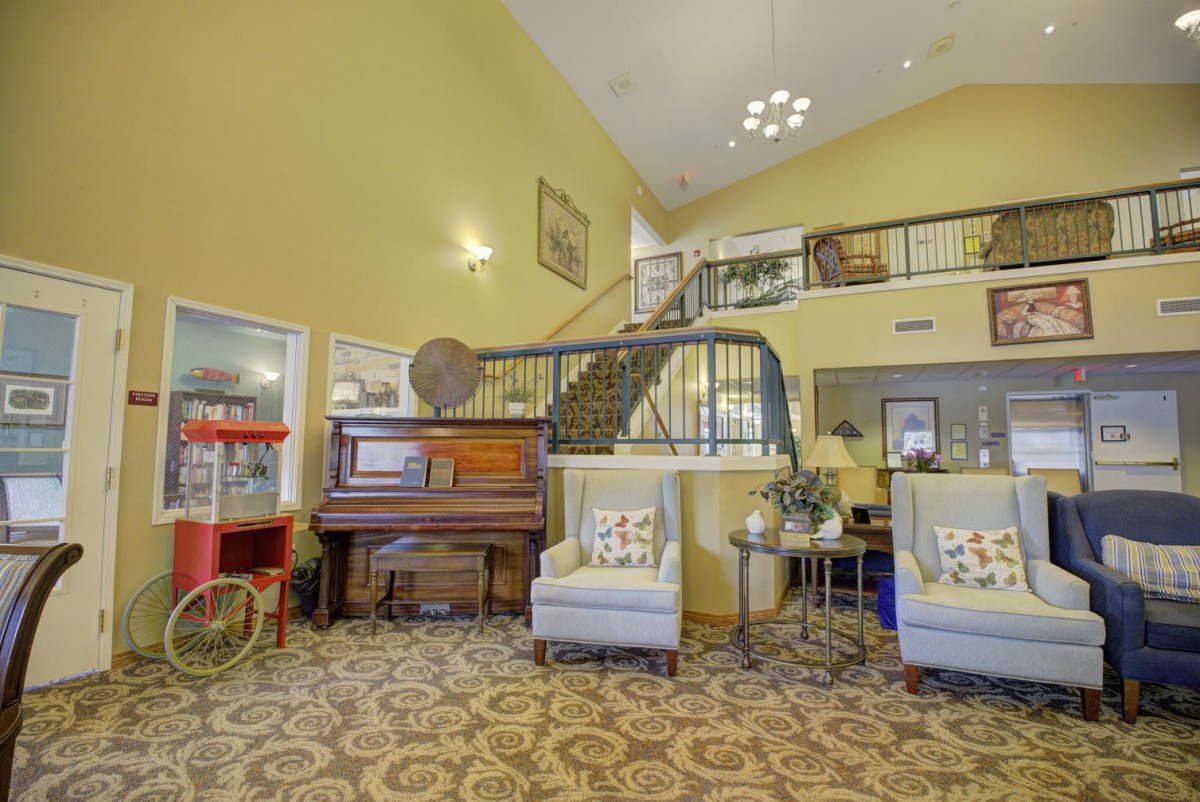 A cozy lobby featuring a piano, armchairs, a popcorn machine, and decorative staircase.