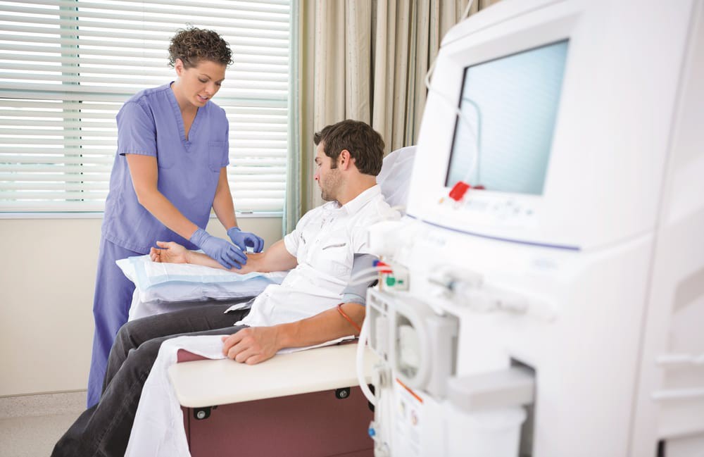 A nurse assists a patient undergoing dialysis treatment with medical equipment in a healthcare setting.