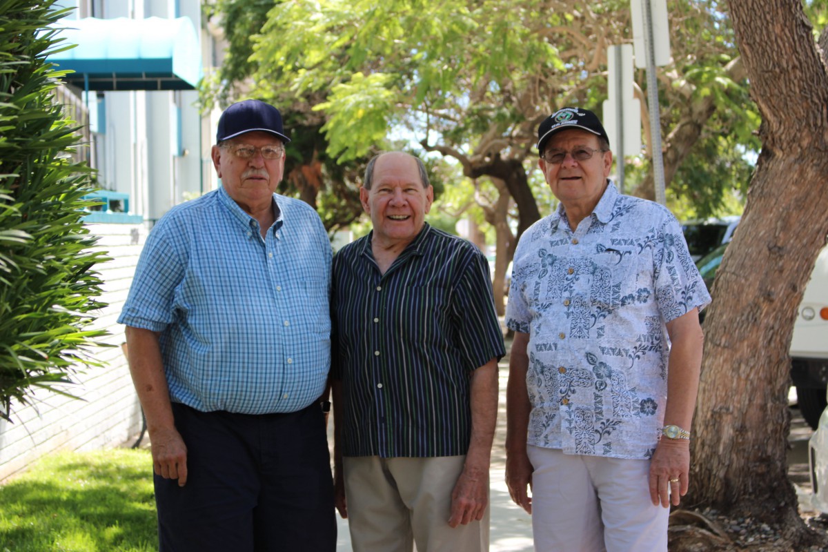 Three men standing together outdoors on a sunny day.