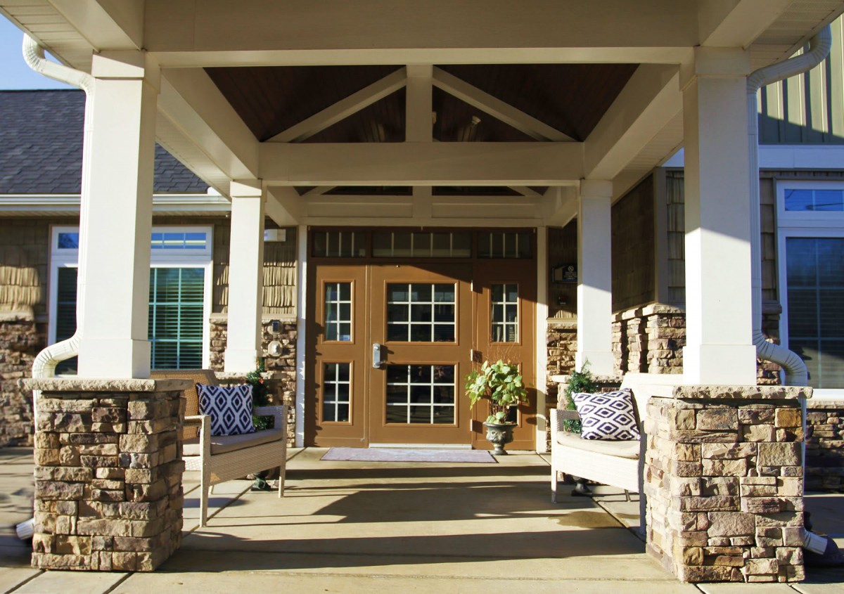 A welcoming front porch with stone columns and a wooden door, featuring outdoor seating.