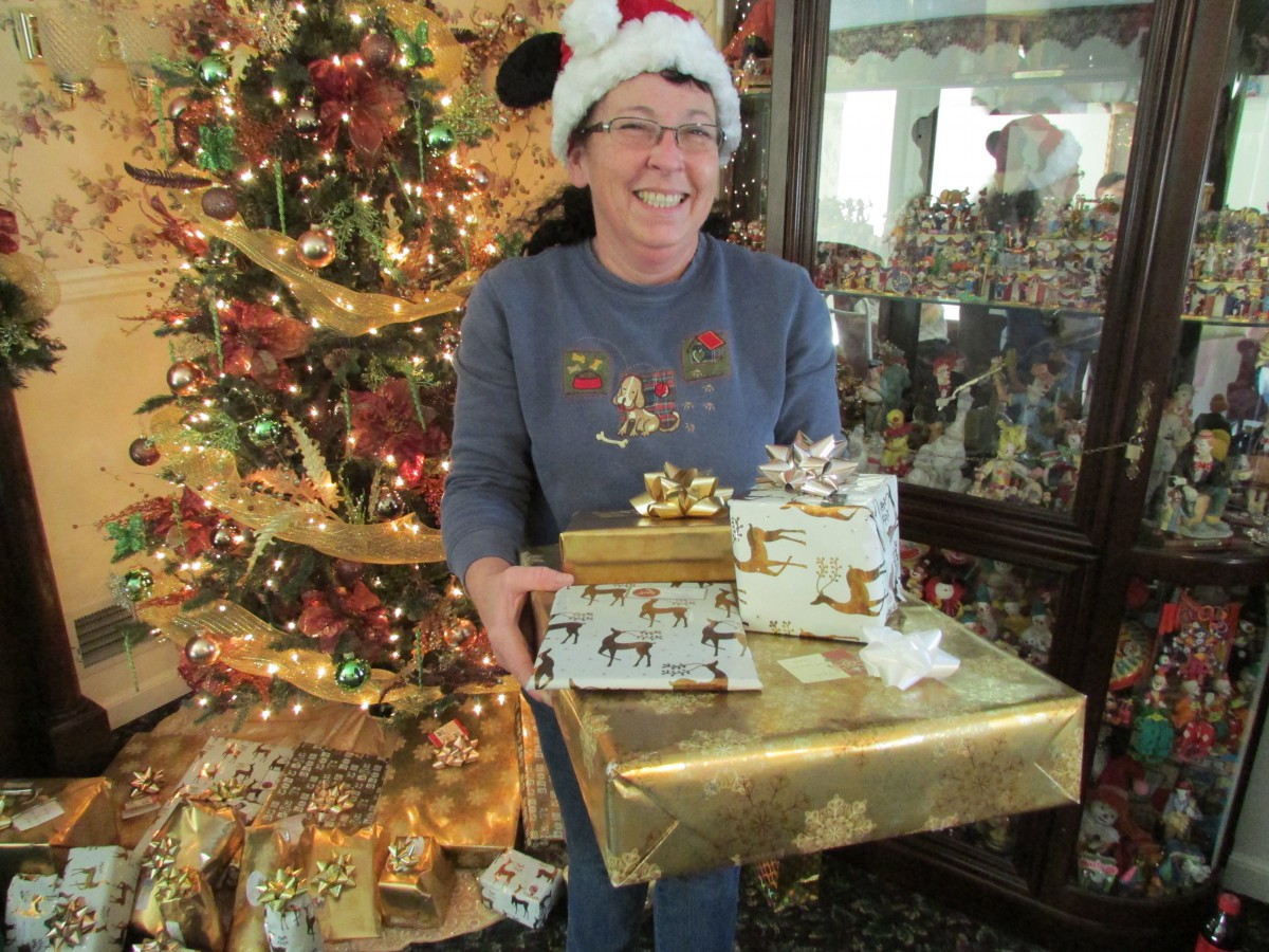 A person holding Christmas presents in front of a decorated tree with a joyful holiday atmosphere.