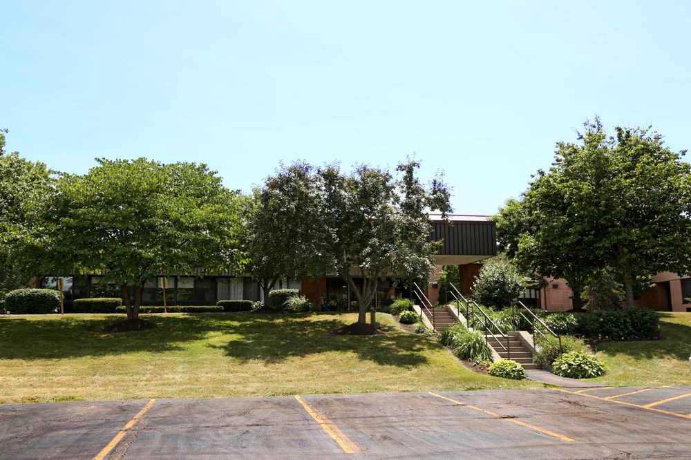 A building surrounded by trees with a parking lot in the foreground.
