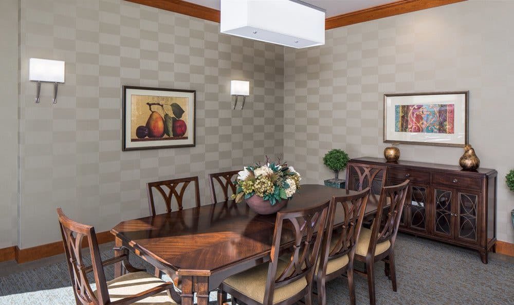 A stylish dining room featuring a long wooden table with matching chairs, elegant wall decor, and ambient lighting.