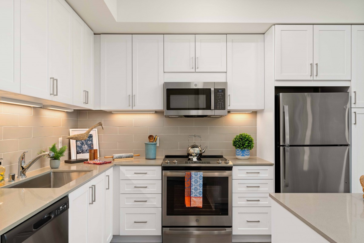 A modern kitchen with white cabinets and stainless steel appliances, featuring a microwave, oven, and refrigerator.