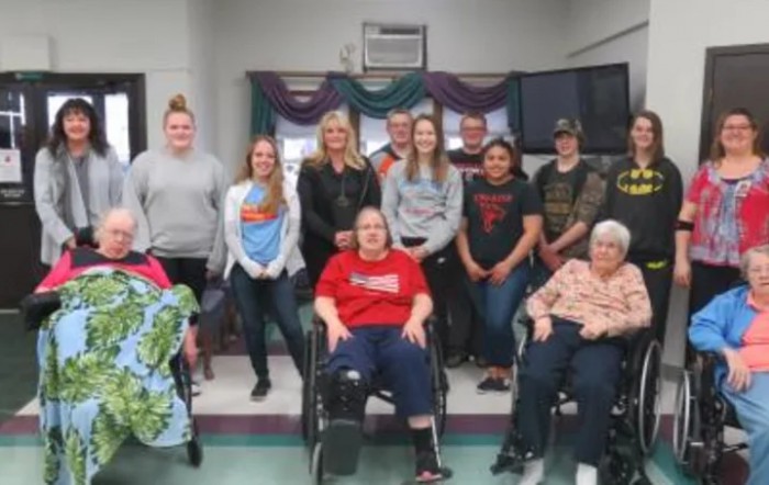 A group of people posed together, with some in wheelchairs, inside a room.