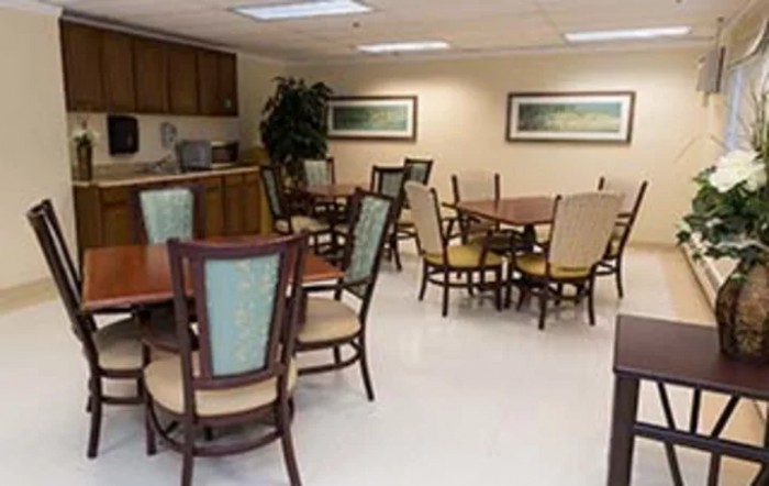 A clean and organized dining area with several tables and chairs, featuring a kitchenette in the background.