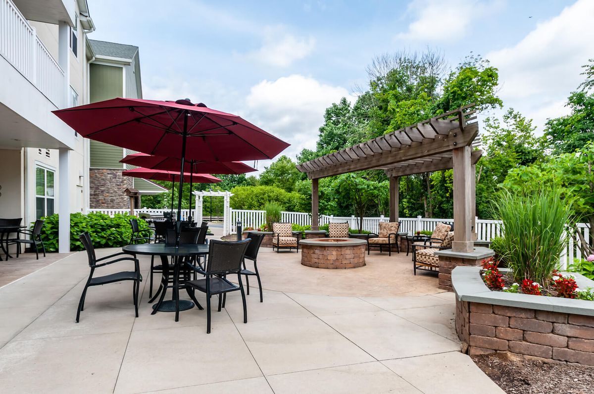 A well-designed outdoor patio featuring a pergola, seating area with umbrellas, and a central fire pit surrounded by lush greenery.