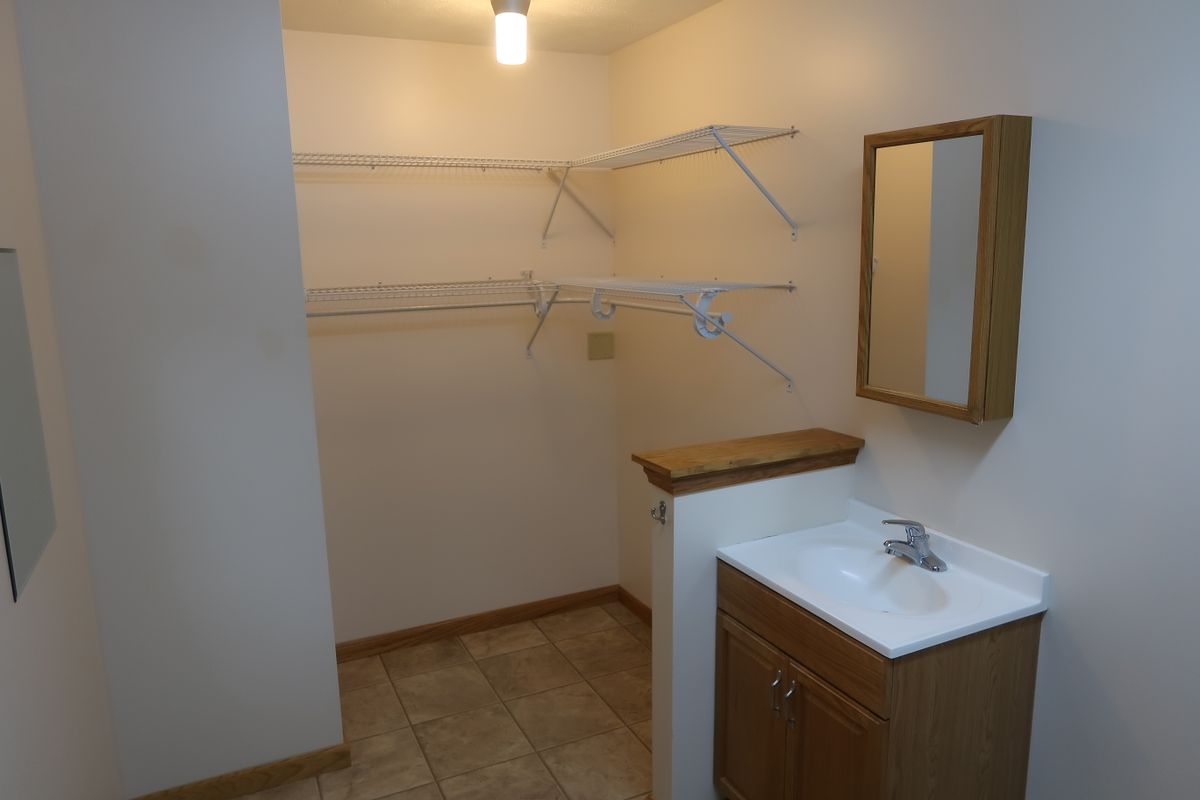 A small room featuring a sink, mirror, and shelving for storage.
