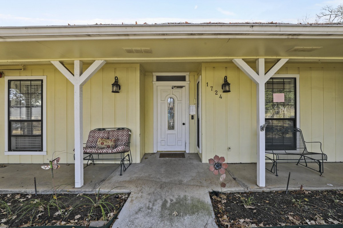 Front entrance of a yellow house with a porch and bench.