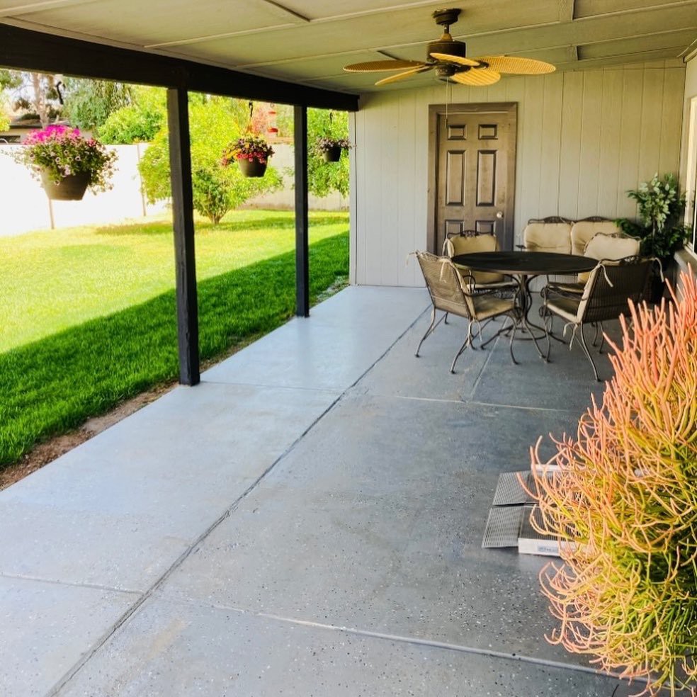 A cozy covered patio with outdoor seating, ceiling fan, and view of a lush garden.