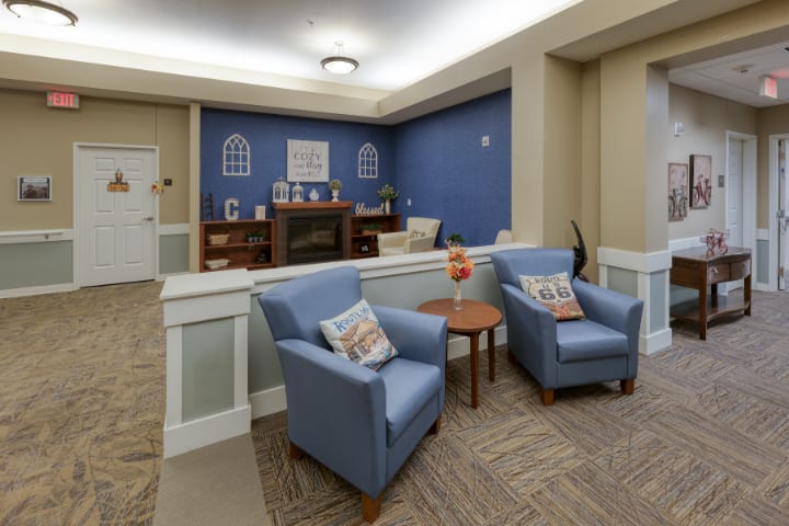 A cozy living room space with blue armchairs, a wooden coffee table, and a fireplace against a blue accent wall.