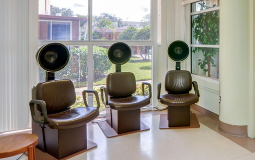 A modern hair salon featuring three stylish chairs with attached hair dryers in a bright, airy space.