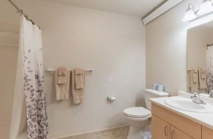A minimalist bathroom with a toilet, sink, and hanging towels in neutral colors.