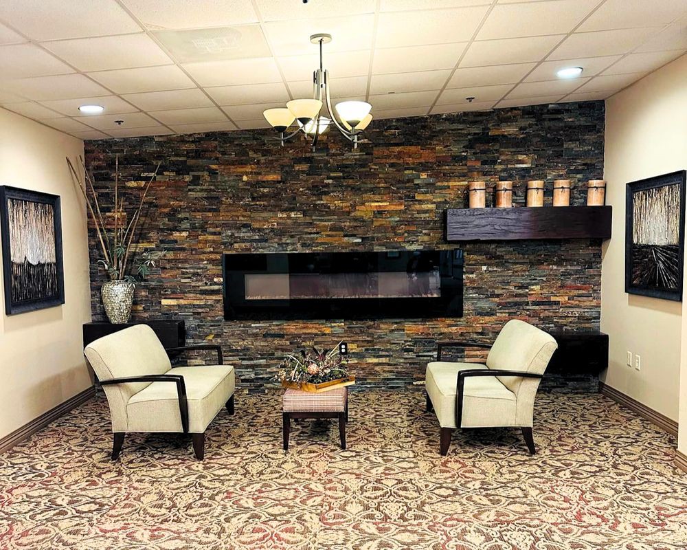 A cozy seating area with two armchairs facing a modern fireplace set against a stone wall.