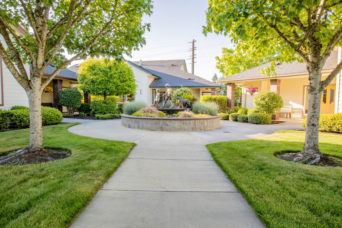 A tranquil garden with a circular pathway surrounded by lush greenery and trees, leading to charming houses.