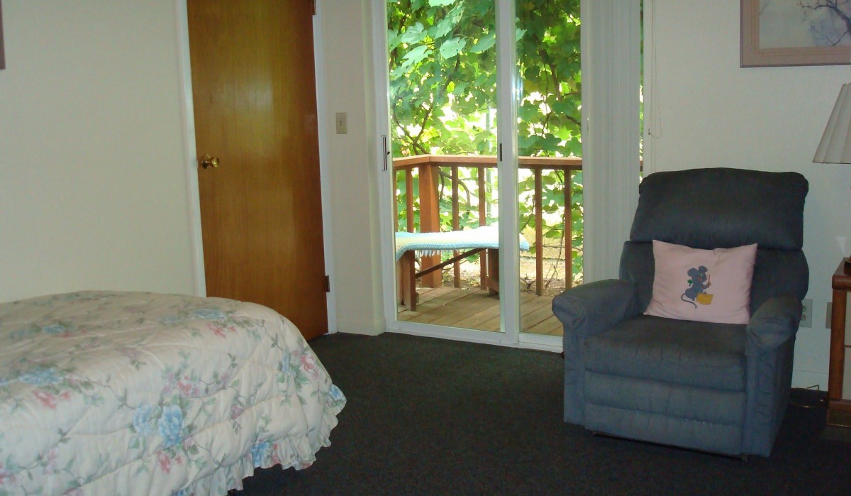 A cozy bedroom with a sliding door leading to a balcony, featuring a comfortable chair and a floral bedspread.