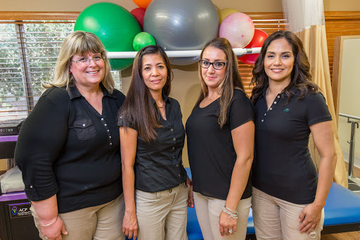 A group of four women standing together in a fitness environment, surrounded by colorful exercise equipment.