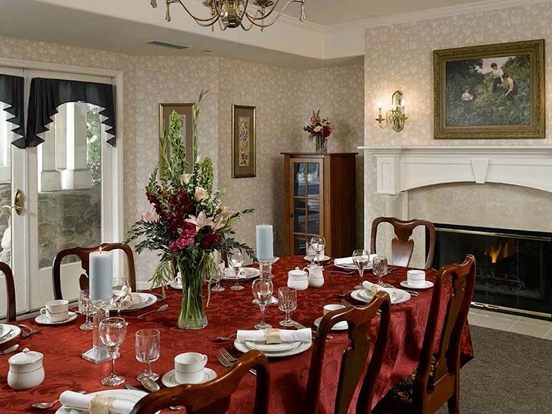 A formal dining room with an elegantly set table featuring a red tablecloth and floral centerpiece.