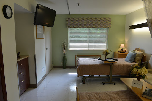 A peaceful hospital patient room featuring two beds, a TV, and natural light coming through the window.