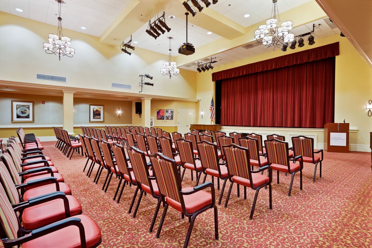 An empty auditorium with rows of chairs facing a stage with red curtains.