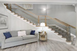 A modern living room featuring a stylish staircase, a comfortable gray sofa, and a cozy lamp on a side table.