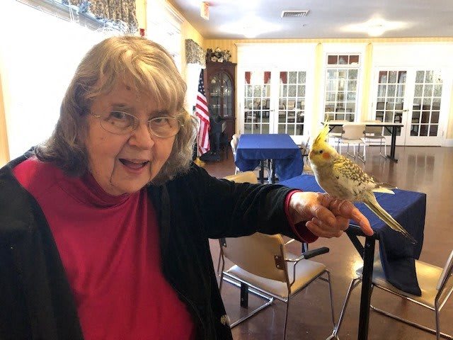 A woman smiling while a cockatiel perches on her hand indoors.