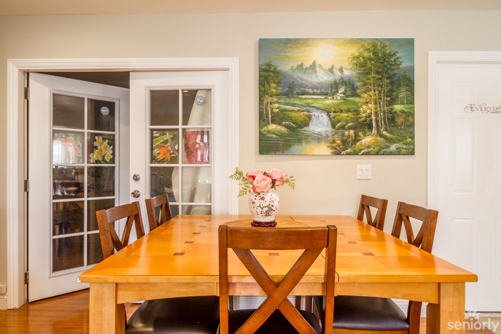 A cozy dining room with a wooden table, chairs, and a landscape painting on the wall.