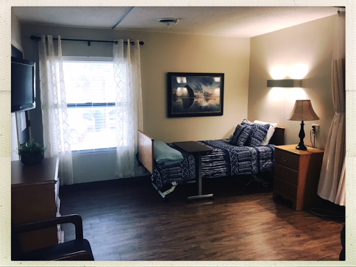 A well-lit patient room featuring a hospital bed, bedside lamp, and a window with sheer curtains.