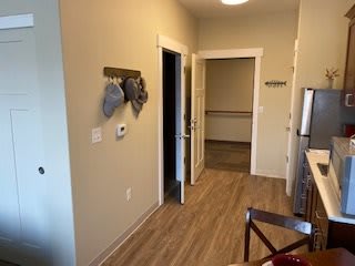 A view of a kitchen hallway with hats hanging on the wall and wooden flooring.