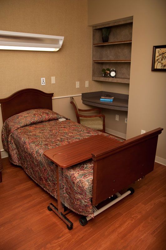 A bedroom with a hospital-style bed, a small desk, and wooden furnishings.