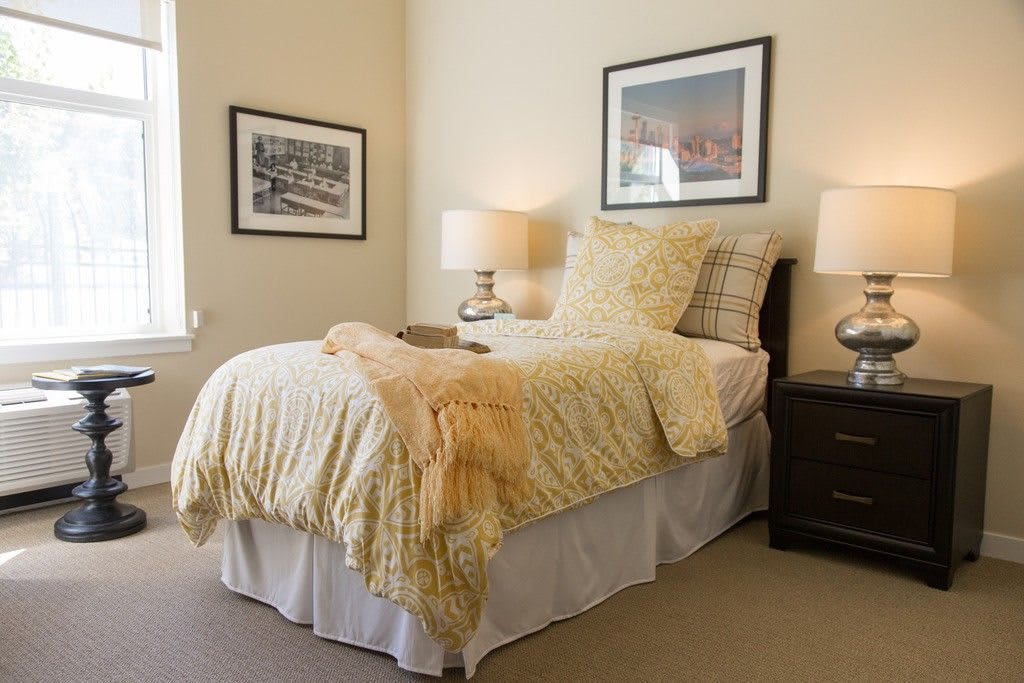 A cozy bedroom with a neatly made bed, two side lamps, and framed artwork on the walls.