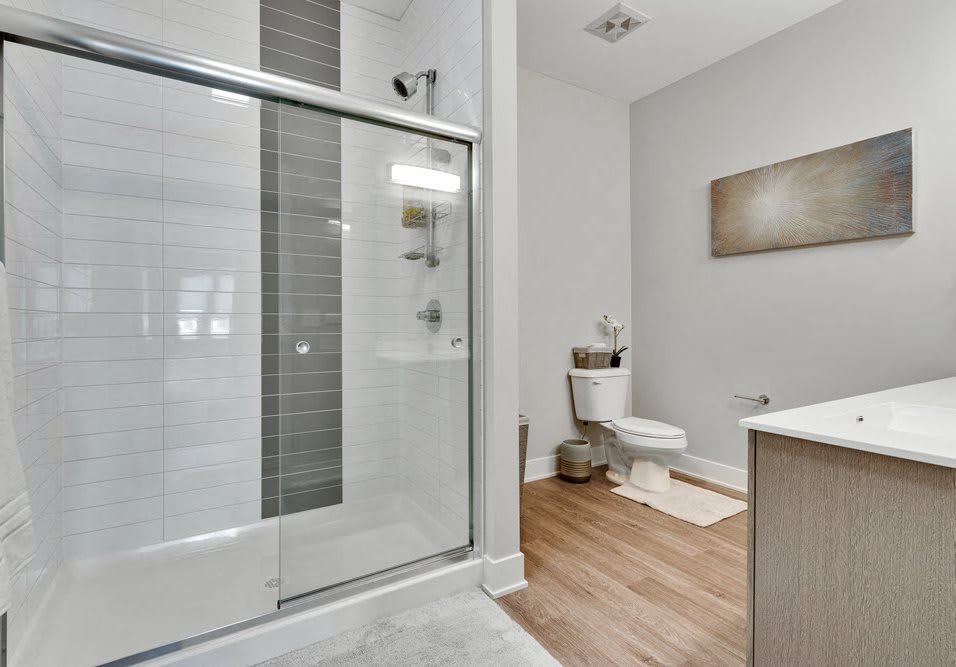 A modern and minimalist bathroom with a glass shower and wooden floor.