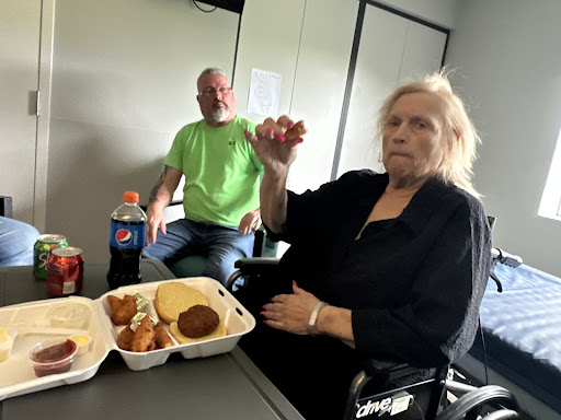 A woman holding food with a man seated in the background, enjoying a meal together.