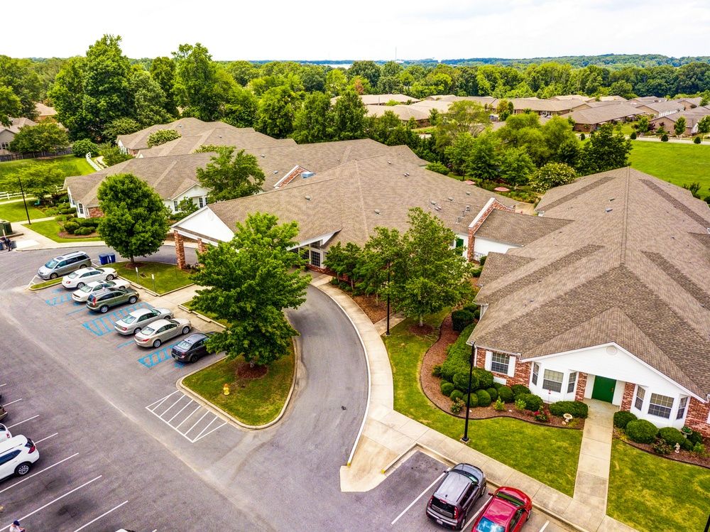 An aerial view of a suburban residential area with buildings, a parking lot, and surrounding trees.