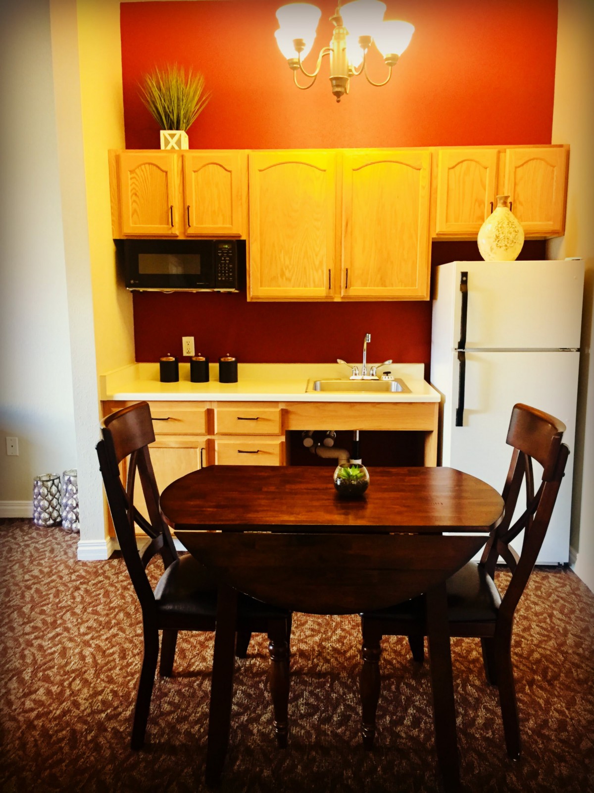 A cozy kitchen and dining area with a wooden table and chairs, featuring light wood cabinets and a refrigerator.
